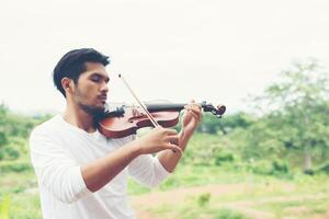 giovane musicista hipster suona il violino nello stile di vita all'aperto della natura dietro la montagna. foto