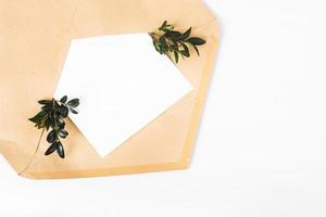 busta di carta artigianale aperta con pezzo di carta vuoto e ramoscelli verdi con foglie isolati su sfondo bianco foto