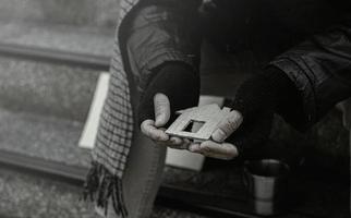 primo piano di un uomo povero o senzatetto, senzatetto, fallito dal lavoro. il povero mendicante della città siede sulle scale con un bicchiere di denaro. foto