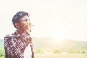 uomo hipster che fuma sigaretta, in piedi dietro una montagna. tra l'aria fresca del mattino. foto