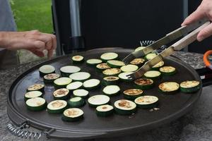 due persone che preparano le zucchine affettate su una griglia. persone irriconoscibili. mani umane foto