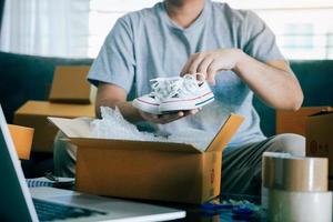 l'adolescente imprenditore asiatico sta trasportando scarpe per bambini e mette in una scatola di cartone il cliente per consegnare il prodotto a casa. foto