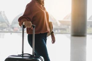 giovani donne e bagagli asiatici del viaggiatore al terminal dell'aeroporto in piedi all'aeroporto tenendo la valigia e camminando nell'aeroporto internazionale. foto