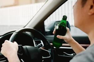 gli uomini asiatici stanno infrangendo le regole del traffico tenendo una bottiglia di birra e bevendo durante la guida. foto