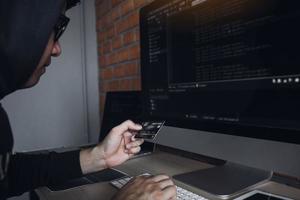 hacker nella cappa che lavora con il computer e tiene una carta di credito con il concetto di hacking dei pagamenti. foto