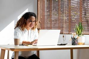 felice giovane donna d'affari afroamericana che lavora da casa sul computer portatile in soggiorno foto