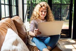 donna caucasica piuttosto sorridente che utilizza il computer portatile sul divano di casa foto