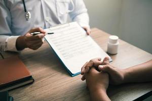 mano del medico che tiene la penna che indica l'elenco della storia del paziente sul blocco note e parla con il paziente di farmaci e trattamenti. foto