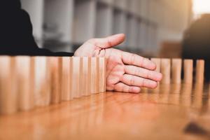 primo piano mano uomo d'affari che impedisce al blocco di legno di cadere nella linea del domino con il concetto di rischio. foto