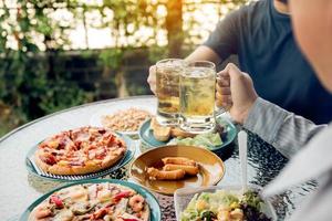 le persone asiatiche stanno socializzando fuori casa con un sacco di cibo sul tavolo e tenendo un bicchiere di birra all'interno tintinnano e si divertono insieme. foto