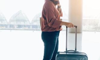 giovane donna asiatica in piedi all'aeroporto tenendo la valigia in aeroporto internazionale a piedi con i bagagli. foto