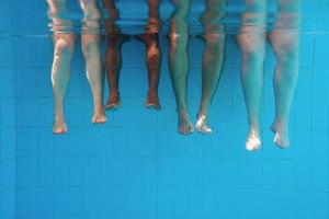 gambe dell'uomo afroamericano con amici caucasici in piscina sott'acqua. estate. concetto di vacanza, internazionale e sportivo. foto