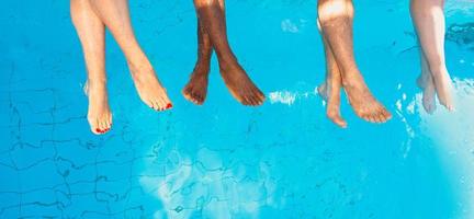 gambe di quattro amici di razza diversa seduti a bordo piscina in una giornata di sole. festa. estate. concetto di vacanza, amicizia internazionale e sport. foto