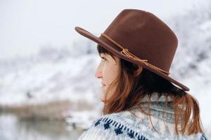 ritratto di una donna con un cappello marrone in feltro e un maglione su uno sfondo di paesaggio invernale foto