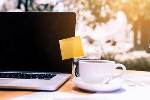 incolla il blocco note appiccicoso sul laptop con una tazza di caffè sulla scrivania in legno. foto