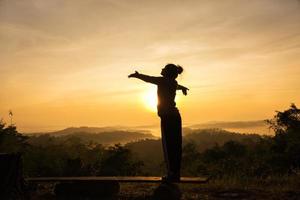 silhouette di donna libera tifo a braccia aperte all'alba del picco di montagna foto