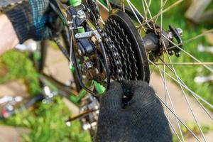 l'uomo meccanico della bici ripara la bicicletta nell'officina di riparazione della bicicletta, all'aperto. la mano del ciclista il ciclista esamina, ripara il moderno sistema di trasmissione del ciclo. manutenzione della bici, concetto di negozio di articoli sportivi. foto