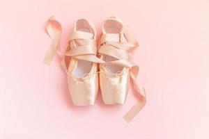 nuove scarpe da ballo beige pastello con nastro di raso isolato su sfondo rosa. ballerine classiche da punta per allenamento di danza. concetto di scuola di danza classica. vista dall'alto distesa, copia spazio foto