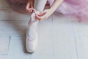 le mani della ballerina mettono le scarpe da punta sulla gamba durante la lezione di ballo foto