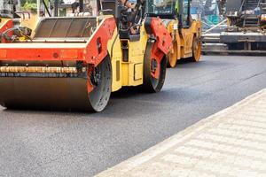 costruzione di una nuova strada, rulli stradali che compattano asfalto fresco sulla strada subito dopo le finitrici in una giornata estiva. foto