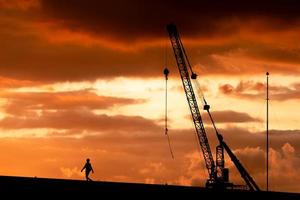 sagoma di un tecnico e gru su sfondo tramonto foto