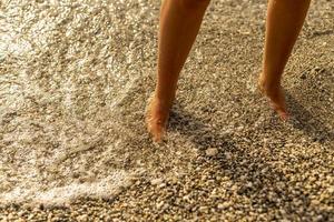 piedi della donna di viaggio del primo piano di rilassarsi sulla spiaggia con l'onda del mare in estate, priorità bassa di feste, concetto di vacanza. foto