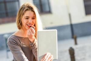 giovane donna che applica rossetto guardando tablet foto