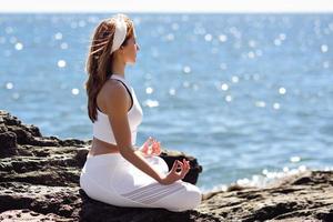 giovane donna che fa yoga in spiaggia indossando abiti bianchi foto