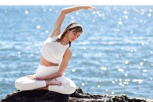 giovane donna che fa yoga in spiaggia indossando abiti bianchi foto