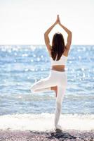 giovane donna che fa yoga in spiaggia indossando abiti bianchi foto