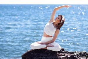 giovane donna che fa yoga in spiaggia indossando abiti bianchi foto