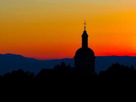la straordinaria bellezza e i colori del tramonto che domina le sagome delle alpi e la sagoma di una bellissima chiesa foto