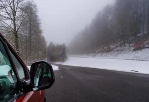 macchina rossa sulla strada invernale in montagna, foresta con neve foto