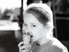 bambina sveglia che mangia il gelato al sole foto