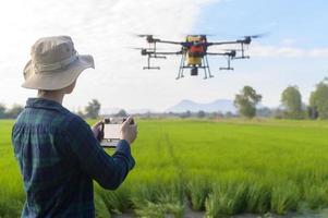 giovane agricoltore intelligente che controlla i droni che spruzzano fertilizzanti e pesticidi su terreni agricoli, innovazioni ad alta tecnologia e agricoltura intelligente foto