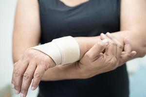 la donna asiatica di mezza età usa la fasciatura elastica per trattare la sindrome di de quervain a portata di mano e il dito in ufficio. foto