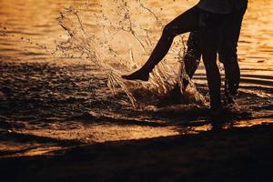 coppia che spruzza i piedi nell'acqua al tramonto foto