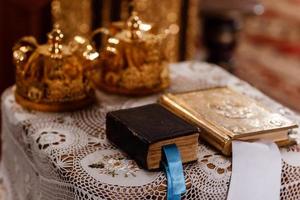 corone d'oro nuziali e Bibbia sul tavolo in chiesa. corone nuziali in chiesa pronte per la cerimonia del matrimonio. avvicinamento. divina liturgia. messa a fuoco selettiva foto