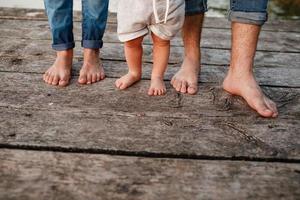 mamma, papà e bambino camminano a piedi nudi sul ponte di legno. felice giovane famiglia trascorrere del tempo insieme, correre fuori, andare nella natura, in vacanza, all'aperto. il concetto di vacanza in famiglia. copia spazio foto