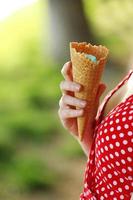 Immagine ravvicinata della mano della donna che tiene il cono di cialda fresco con gelato alla vaniglia e lampone sullo sfondo di legno. foto