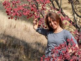 donna sorridente vicino a un albero con foglie rosse, ritratto autunnale foto