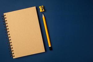 taccuino marrone con vista dall'alto con matita gialla e blocco note sul tavolo da lavoro blu navy foto
