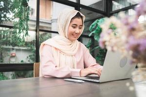 bella giovane donna musulmana asiatica sorridente che lavora al computer portatile che si siede nel soggiorno di casa. Asian business woman documento di lavoro finanza e calcolatrice nel suo ufficio a casa. godersi il tempo a casa. foto