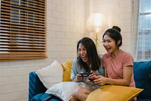 le coppie di donne lesbiche lgbt giocano a casa, femmine asiatiche usando il joystick che hanno un momento felice divertente insieme sul divano nel soggiorno di notte. giovane tifoso amante del calcio, celebra il concetto di vacanza. foto