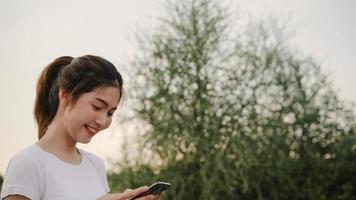 allegro asiatico turista blogger donna utilizzando la tecnologia touchscreen allo smartphone mentre si cammina per strada al centro città la sera. concetto di vacanza viaggio turistico zaino stile di vita. foto