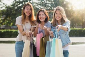 gruppo di giovane donna asiatica che acquista in un mercato all'aperto con le borse della spesa nelle loro mani. le giovani donne asiatiche mostrano ciò che hanno nella borsa della spesa sotto la calda luce del sole. concetto di shopping all'aperto di gruppo. foto