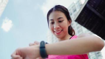 sana bella giovane donna atleta asiatico impostazione e controllo dei progressi guardando il cardiofrequenzimetro su smart watch durante l'esecuzione in città urbana. le donne di stile di vita esercitano nel concetto di città. foto