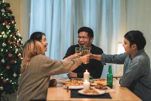 buon natale e felice anno nuovo gruppo di giovani amici a cena a casa. festa di famiglia asiatica con birra e pizza vicino all'albero di natale a casa di notte. festa di celebrazione e stare insieme. foto