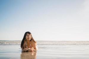 giovane donna asiatica che si sente felice sulla spiaggia, bella femmina felice rilassarsi sorridente divertimento sulla spiaggia vicino al mare quando il tramonto in serata. stile di vita le donne viaggiano sul concetto di spiaggia. foto