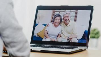 giovane donna asiatica d'affari che utilizza la videochiamata del laptop parlando con il papà e la mamma di famiglia mentre lavora da casa nella camera da letto. autoisolamento, distanziamento sociale, quarantena per la prevenzione del virus corona. foto